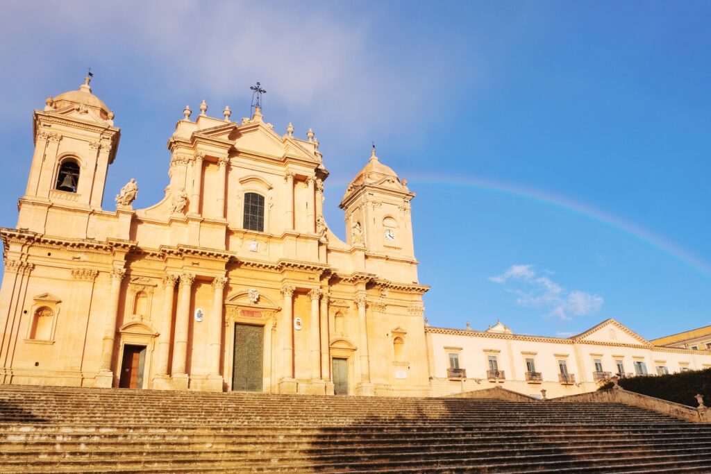 View of Noto Cathedral with a faint rainbow overhead after a rainy winter afternoon.