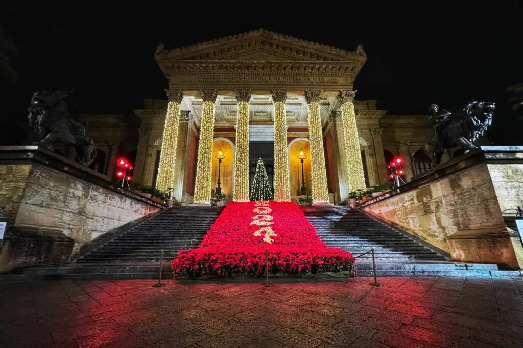 Teatro Massimo at night lit with Christmas lights and red poinsettias on the stairs