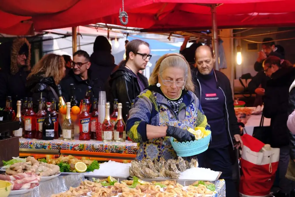 Woman serving fried seafood and oysters at a street food stall in Ballarò Market, Palermo