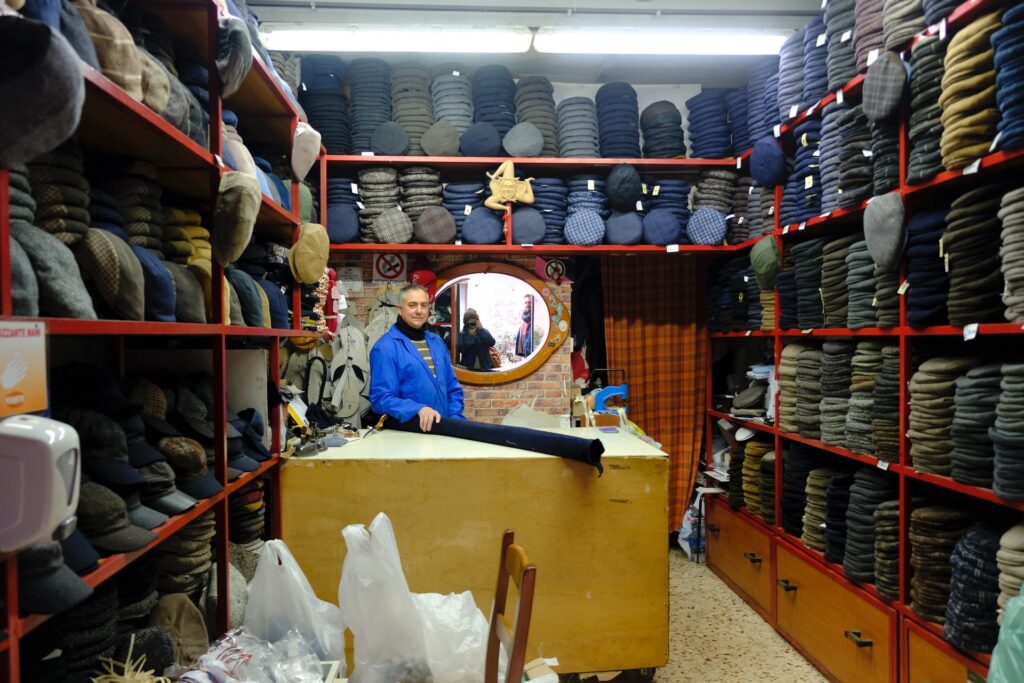 Shop Owner at Mascari Francesco in Palermo, surrounded by walls of traditional Sicilian coppola hats