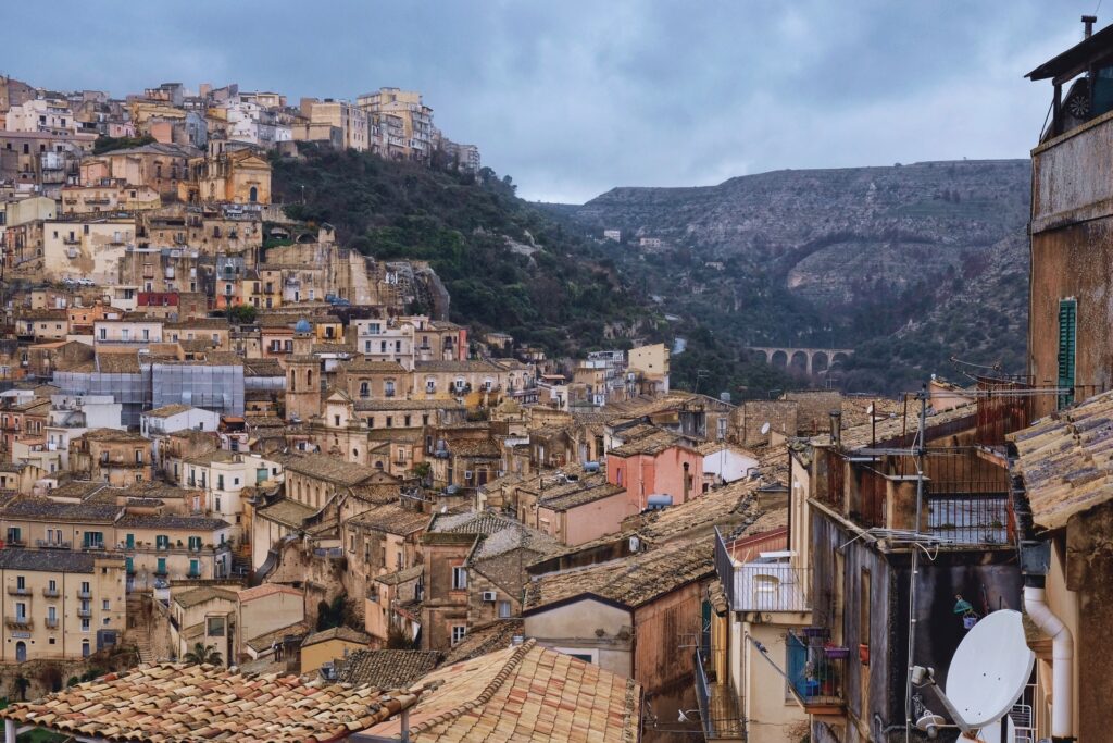 View of Ragusa Ibla in southeastern Sicily, showing stacked stone houses tumbling down the hillside under foggy winter skies.