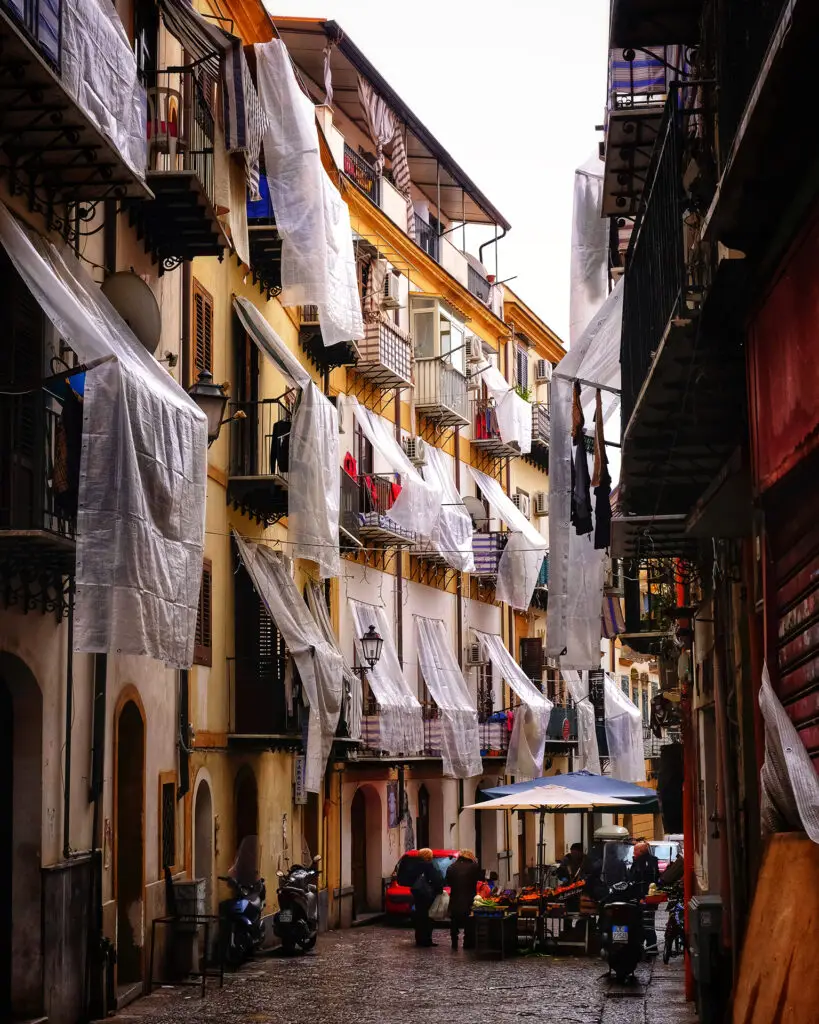 Market stalls beneath balconies along a narrow street at Capo Market in Palermo