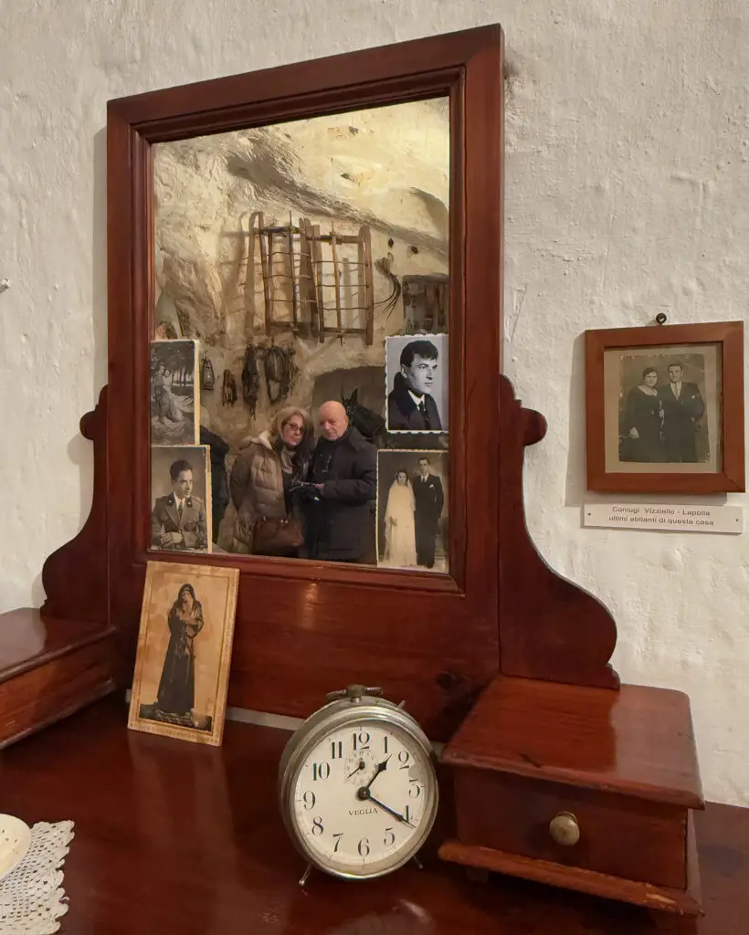 Old family photographs, wooden mirror and alarm clock inside a Matera cave house