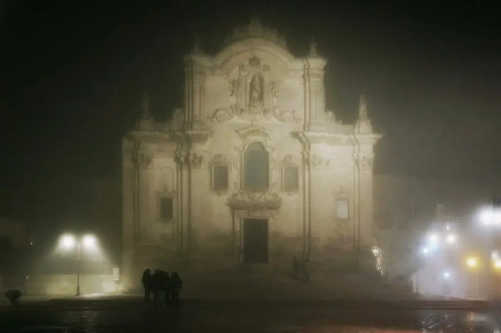 A church façade barely visible through fog in Matera at night