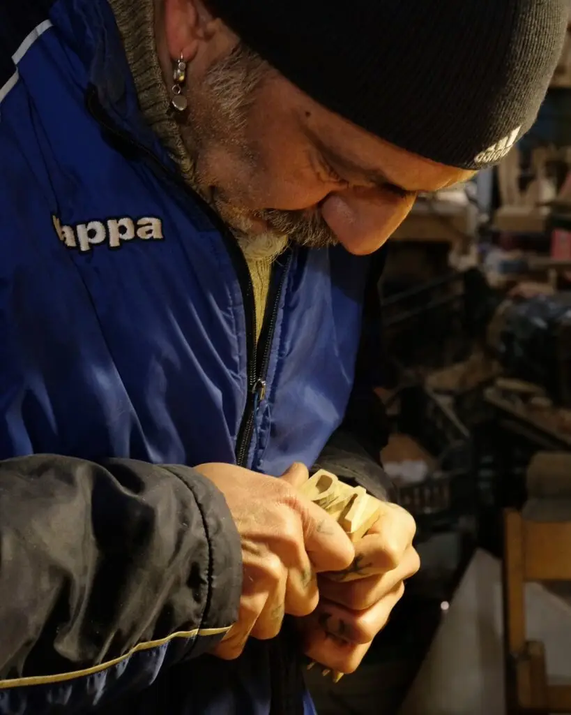 Giuseppe carving Dewi’s initials into the base of an olive-wood rooster in Matera