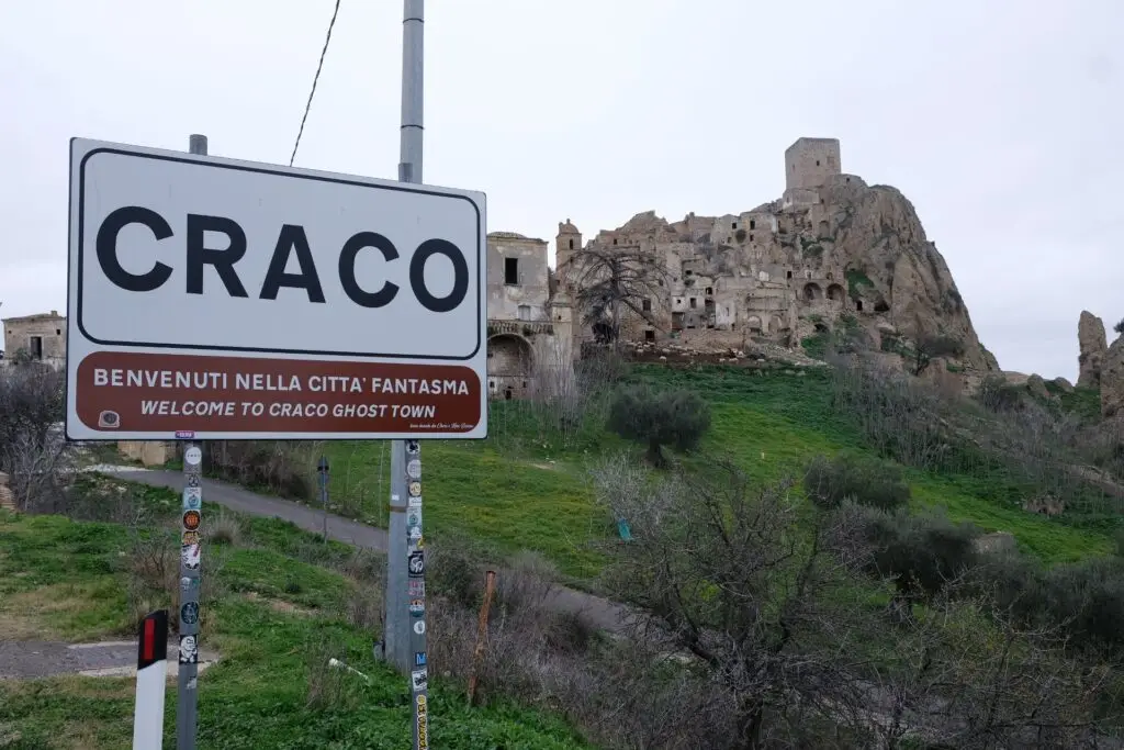 Welcome to Craco ghost town sign with the abandoned town behind it
